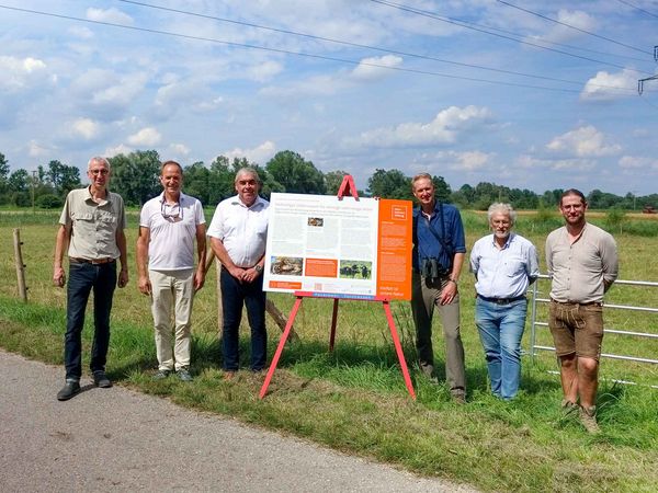 Mehrere Personen stehen neben einem Infoschild vor einer Weidefläche.